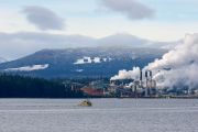 Workboat collecting stray logs near Gabriola Island with Harnac pulp mill Nanaimo in background British Columbia Canada